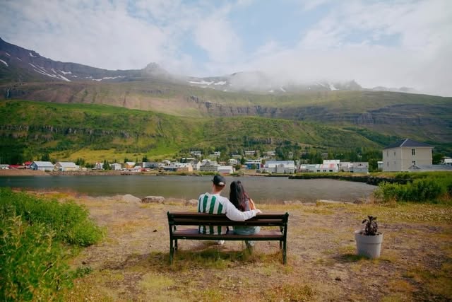 Couple on a bench looking across a fjord toward a mountain village