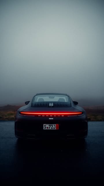 Rear of a Porsche 911, taillight bar glowing through highland fog